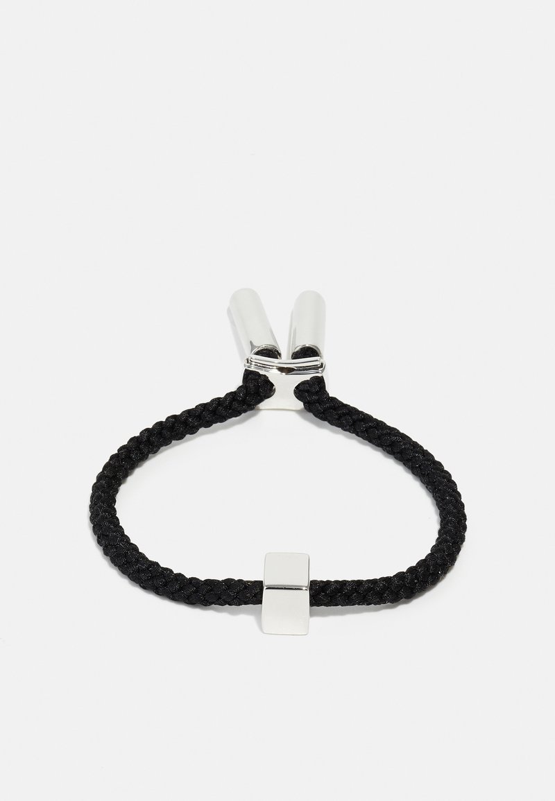 Élastique à cheveux noir avec un détail en métal argenté rectangulaire. La texture est lisse, contrastant avec le matériau tissé.