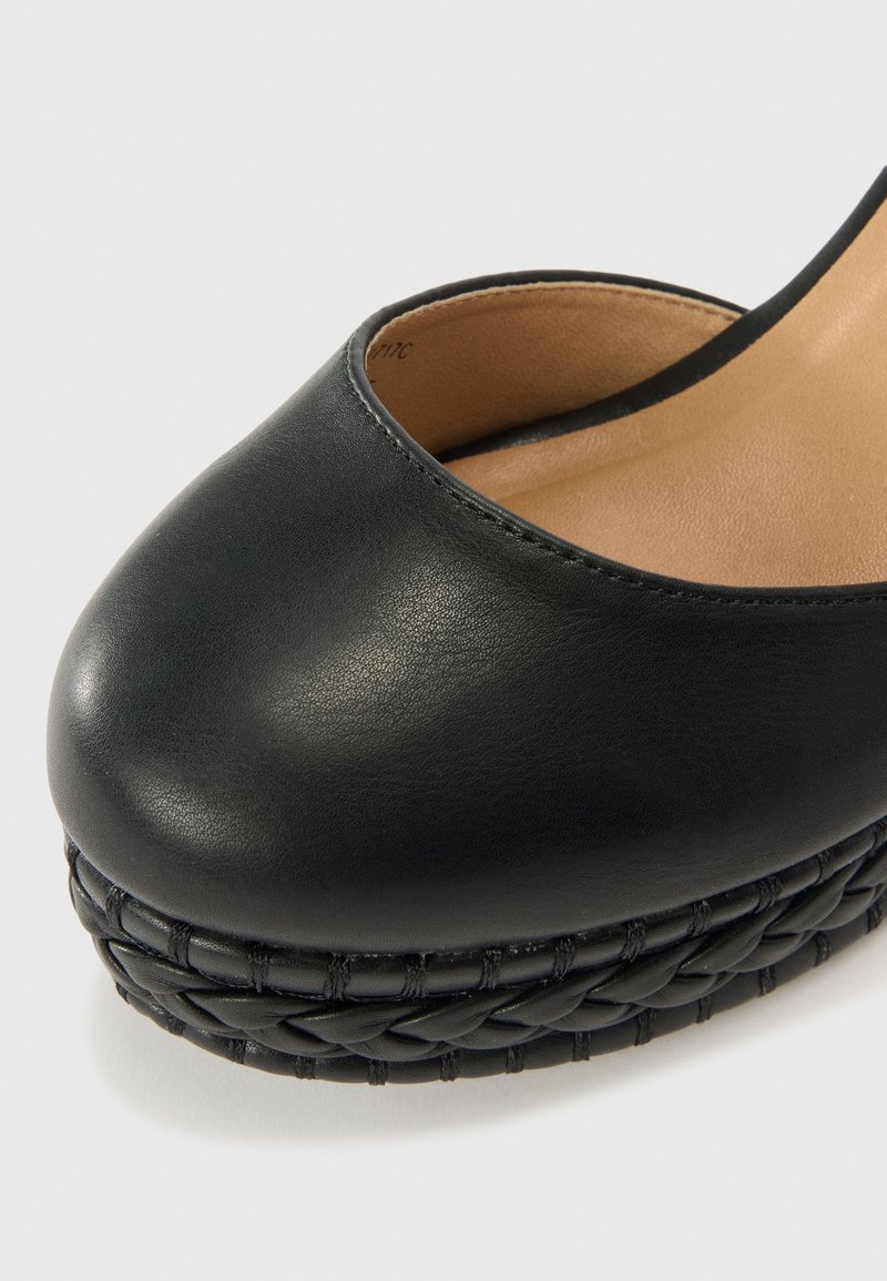 Chaussure à plateforme en cuir noir avec un bout arrondi, texture lisse, et une base tissée texturée. L'intérieur est doublé de beige.