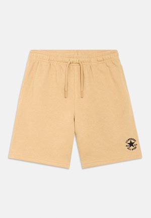 Shorts beiges en coton avec une taille élastique et un cordon de serrage. Présente un logo noir sur le côté gauche inférieur. Texture lisse, coupe au niveau des genoux.