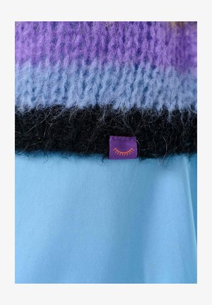 Sweter dzianinowy w kolorze fioletowym, niebieskim i czarnym o miękkiej teksturze. Posiada wszytą fioletową metkę z pomarańczowym wzorem słońca na dole.