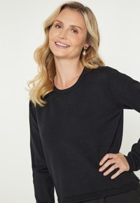 Pulover negru din tricot, cu decolteu rotund, mâneci lungi și manșete cu striații. Prezintă o croială ușor relaxată și slituri laterale la tiv.