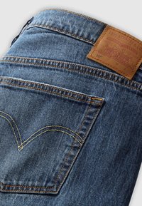 Poche arrière et ceinture d'un jean denim bleu Levi's, montrant des coutures orange et une étiquette de marque en cuir marron.