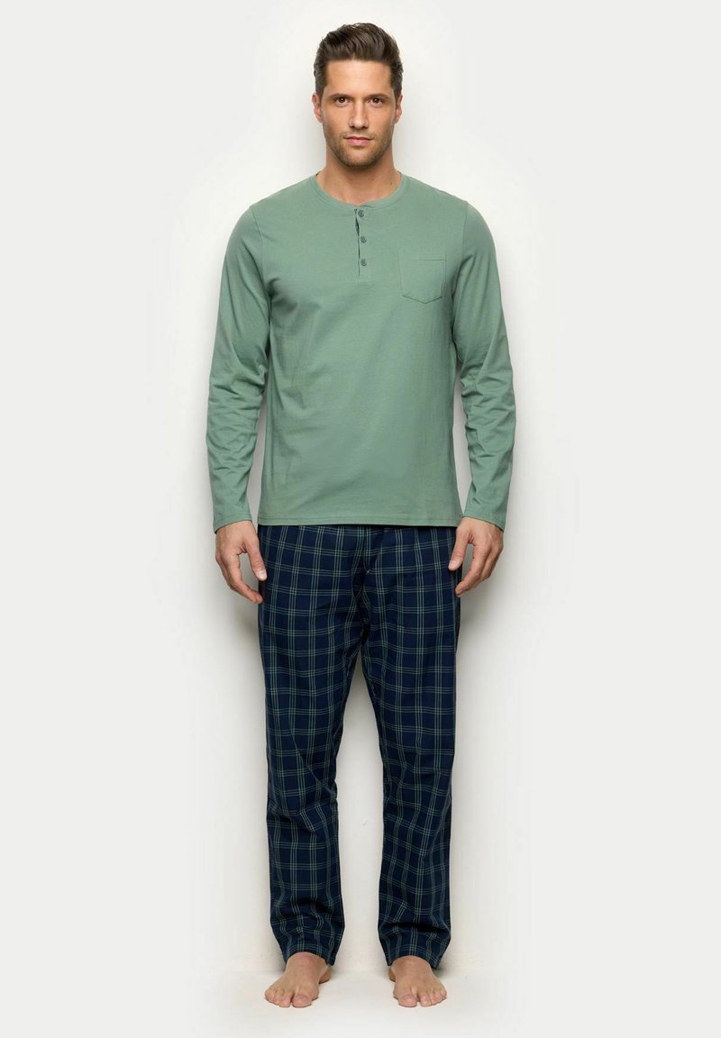 Pitkähihainen vaaleanvihreä puuvillatoppi, jossa on rintatasku ja kolme nappia. Laivastonsiniset ruutuhousut vihreillä yksityiskohdilla ja kuminauhavyötäröllä.