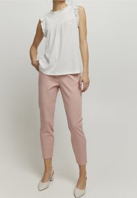 Vit, texturerad topp med volangdetaljer; kombinerad med ljusrosa, slim-fit byxor. Bärs med krämfärgade skor med blockklack.