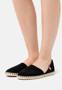 Espadrilles de ante negro con punta redondeada, suela intermedia de yute trenzado y costuras negras a lo largo del borde. Diseño minimalista sin hebillas, tipo slip-on.