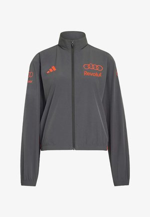 Ciemnoszara kurtka na zamek z wysokim kołnierzem, pomarańczowe logo Adidas po lewej stronie klatki piersiowej, pomarańczowe logo Audi i Revolut na klatce piersiowej i rękawach.