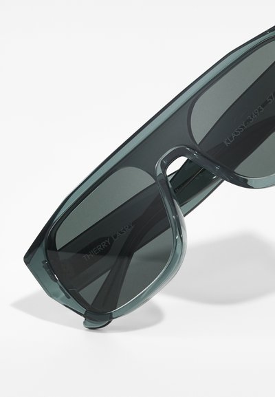 Occhiali da sole con lenti nere, montatura trasparente e forma angolare, tinti di verde. Marchio inciso sulla parte interna della asta.