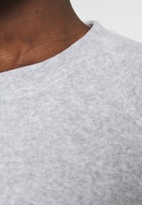 Sudadera gris claro con un tejido suave y texturizado. Cuenta con un escote redondo y detalles de costuras visibles. Vista en primer plano que muestra la calidad del tejido.