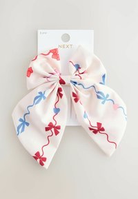 Un nœud en tissu doux, avec un fond rose clair orné de rubans bleus et rouges, de cœurs et de nœuds dans un motif répétitif.