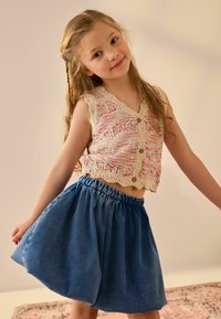 Top senza maniche in maglia con motivo colorato e bordi a scallop; abbinato a una gonna in denim blu con cintura elastica e forma svasata.