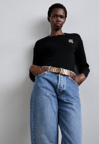 Μαύρο ριμπ πουλόβερ με χρυσό κονκάρδα αρκούδας, συνδυασμένο με ανοιχτό μπλε ψηλόμεσες τζιν και καφέ ζώνη με μεγάλη χρυσή πόρπη "MOSCHINO".