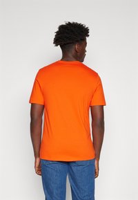 Oranges Kurzarm-T-Shirt mit Rundhalsausschnitt, mit glatter Textur und taillierter Passform, kombiniert mit blauen Jeans.