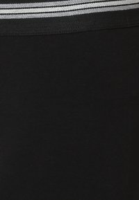 Svart tyg har en bred, texturerad midjeband med tre horisontella silverstripes. Den övergripande designen är enkel och monokromatisk.