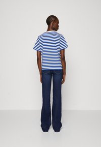 Blå og hvid stribet t-shirt med korte ærmer, parret med mørkeblå klokkerjeans. Materialerne synes at være bomuld og denim.