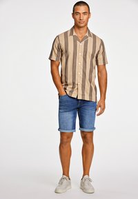 Camisa de manga corta a rayas en beige y marrón con cuello tipo pico, combinada con pantalones cortos de mezclilla con dobladillo enrollado y zapatillas ligeras.