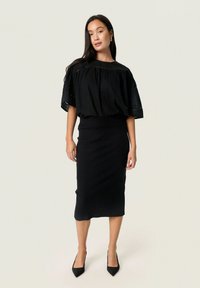 Haut noir à manches courtes, à coupe ample, avec un tissu texturé et un col rond. Assorti à une jupe midi noire à côtes ajustée et à des talons aiguilles.