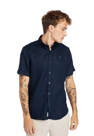 Camicetta a maniche corte colore navy, con bottoni, realizzata in tessuto texturizzato e con un piccolo logo sul petto, caratterizzata da un colletto classico e chiusura a bottoni.