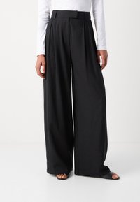 Mustat leveät housut korkealla vyötäröllä ja poimutuksilla, valmistettu kevyestä kankaasta. Sujuva pinta ja minimaalinen sauman määrä. Yhdistetty mustiin sandaaleihin.