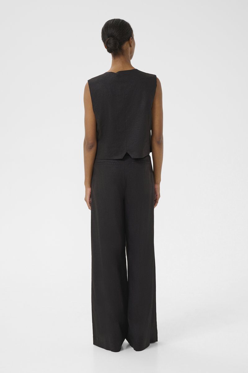 Czarny bezrękawnik o okrągłym dekolcie i rozcięciu z tyłu, zestawiony z szerokimi spodniami w dopasowanym materiale, tworząc minimalistyczny wygląd.