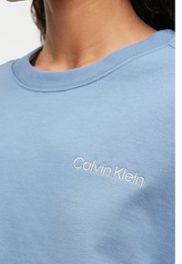 Ανοιχτό μπλε sweatshirt με ριγέ λαιμό και κεντημένο λογότυπο "Calvin Klein" σε λευκό στο στήθος. Λείο υλικό από βαμβακερό μείγμα.