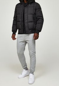 Sort dunjakke med hætte og lynlås, med sidelommer og ribstrikkede manchetter. Kombination med grå joggingbukser og hvide sneakers.