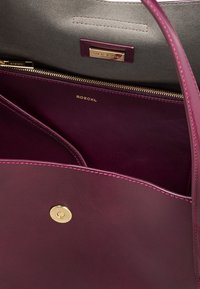 Burgundy leather handbag with gold hardware, featuring a zippered interior and pink stitching. Lined with gray fabric, includes brand label.