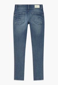 Jeans de mezclilla azul ajustados con un lavado desteñido, que cuentan con dos bolsillos traseros con costuras decorativas y una etiqueta en la cinturilla.