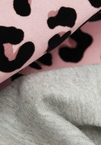 Zwei Stoffmuster: eines in Pink mit schwarzen, flauschigen Leopardenflecken, das andere in hellgrauem Strick, das eine weiche Textur und kontrastierende Muster zeigt.