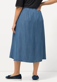 Falda de mezclilla de azul medio, hasta los tobillos, con cintura elástica, textura suave y detalles de costura sutiles en el dobladillo.