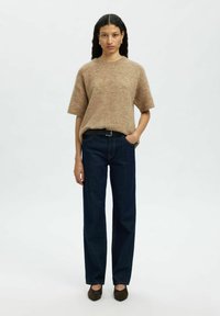Un pull marron à manches courtes avec une texture douce, associé à un jean droit taille haute bleu foncé et des talons marron foncé.