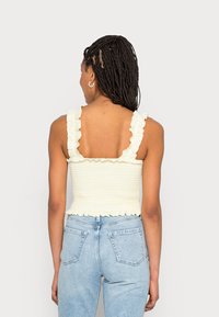 Top cropped amarelo com pregas e alças com rendas, tecido texturizado, e silhueta ajustada, combinado com jeans azuis de cintura alta.