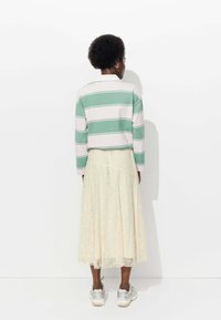 Haut rayé vert et blanc à manches longues associé à une jupe midi en dentelle crème, présentant un design évasé et des baskets métalliques.
