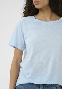 Ljusblå T-shirt i mjukt tyg, med rund halsringning, korta ärmar och en avslappnad passform. Något texturerad yta.