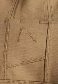 Gros plan d'un tissu beige avec des coutures détaillées et un motif subtil en forme de triangle cousu au centre.