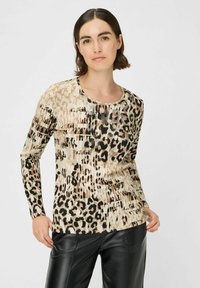 Langärmliges Oberteil mit einem beigen und schwarzen Leopardenmuster, aus strukturiertem Stoff und einem runden Ausschnitt. Kombiniert mit schwarzen Lederhosen.