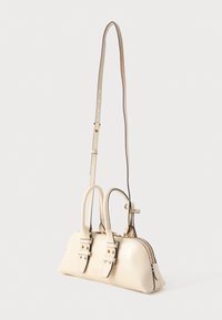 Krém színű bőr kézitáska két felső fogantyúval, állítható, hosszú vállpánttal, arany színű csatokkal és felső cipzáras zárással.
