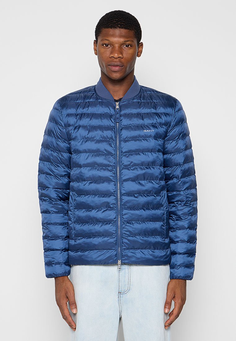 Granatowa kurtka puchowa z zapięciem na zamek, prążkowanym kołnierzem oraz poziomym pikowaniem. Wykonana z błyszczącego materiału o lekkiej teksturze.