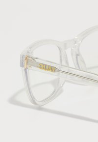 Gafas de gran tamaño con montura transparente. Las varillas de metal acentuadas en dorado presentan el nombre de la marca grabado "QUAY". Textura suave.