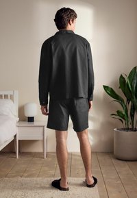 Dark gray, long-sleeve shirt paired with matching shorts, made of soft material. Plain design with buttons, worn with slippers, in a neutral room.