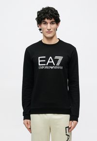 Μαύρο φούτερ με το λογότυπο «EA7 EMPORIO ARMANI» σε λευκό και ριγέ σχέδιο. Στρογγυλή λαιμόκοψη με μακριά μανίκια, μαλακή υφή.