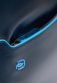 Bolso de cuero azul marino con una textura suave, que presenta una cremallera y costuras azules. El interior muestra un vistazo de elementos organizativos.