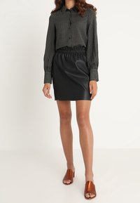 Mustavalkoraidallinen nappikiinnitteinen paita, elastisella vyötärönauhalla varustettu keinonahkainen hame ja ruskeat avokärkiset korkokengät. Tasoittu pinta koko asussa.