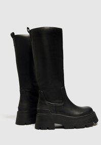 Knee-high black leather boots with a chunky platform sole, featuring a rounded toe and pull tabs at the top for easy wear.