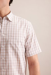 Camicia a maniche corte con bottoni in beige chiaro con un motivo a tartan. Presenta una tasca sul petto e una texture di tessuto liscia e traspirante.