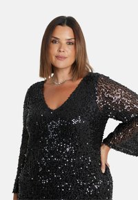 Černé šaty se flitry, s výstřihem do V a dlouhými průhlednými rukávy s lesklou texturou, navržené pro přiléhavý střih.