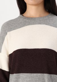 Sweter dzianinowy z naprzemiennymi paskami w kolorach szarym, kremowym i bordowym. Żebrowana faktura i klasyczny okrągły dekolt. Miękki materiał.