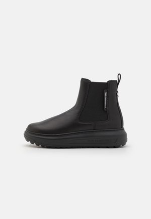 Boots en cuir noir avec panneau latéral élastique, languette à l'arrière, semelle épaisse et petite étiquette de marque sur le côté extérieur.