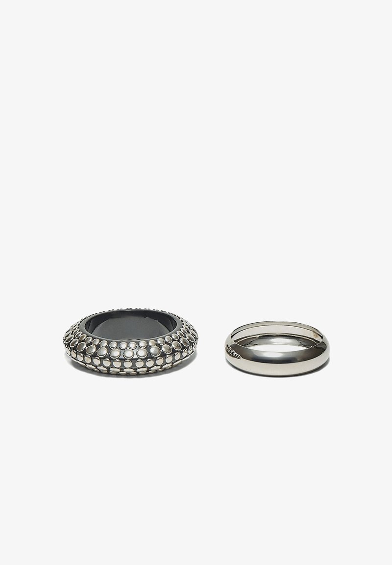 Deux bagues en argent sur une surface blanche ; l'une présente une texture ponctuée tandis que l'autre est lisse et polie.