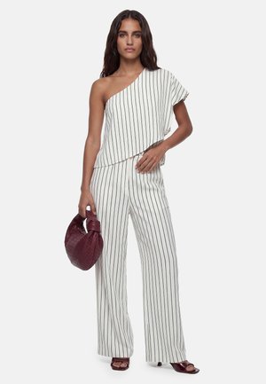 Woman wearing white one-shoulder top and matching wide-leg pants with black vertical stripes, holding a burgundy woven handbag.