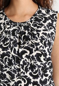 Zwart-wit stoffen met een bloemenpatroon en een geplooide halslijn. Het ontwerp bevat gedurfde, kronkelige bladeren en een zachte textuur.